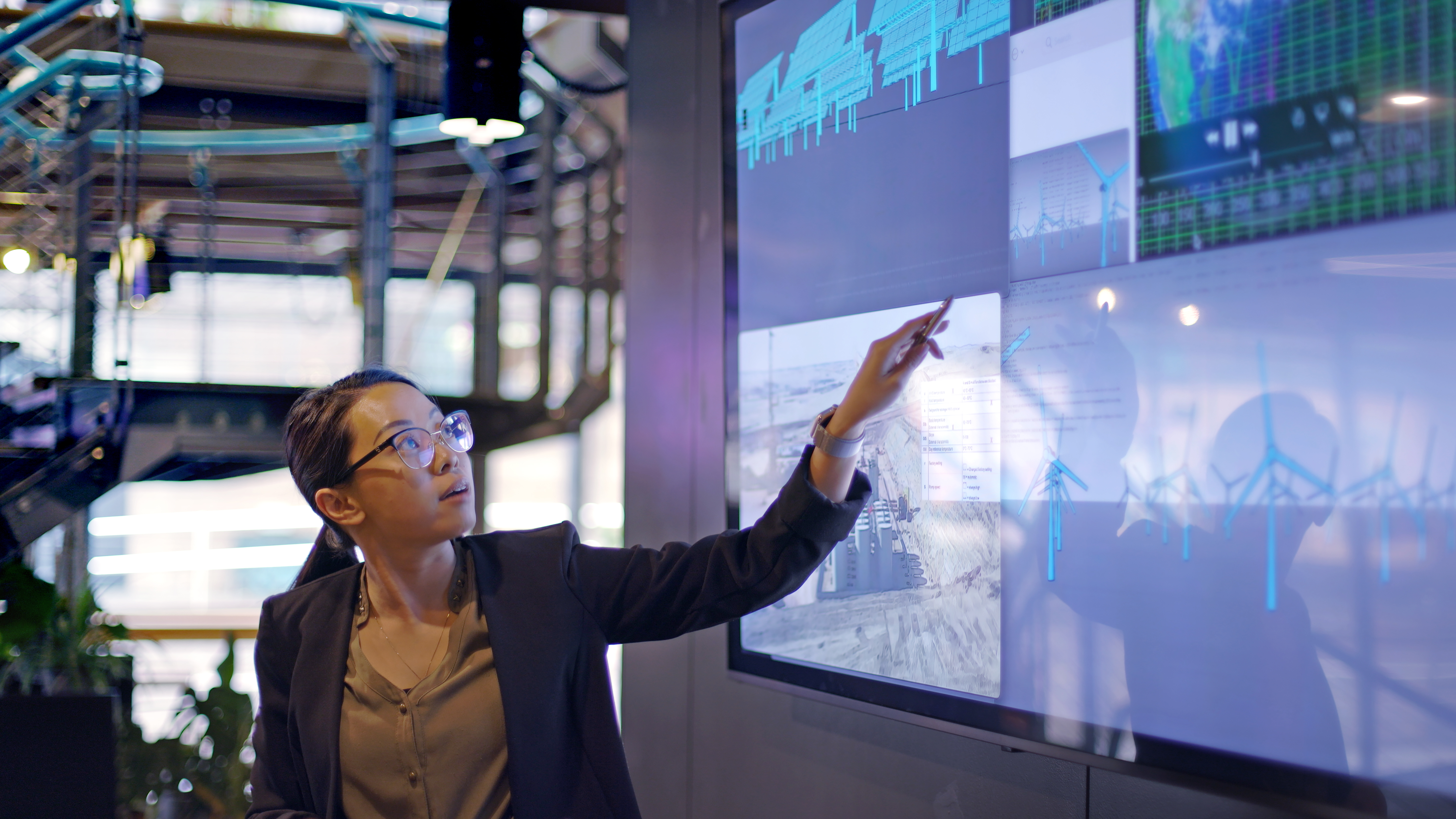 Screen displaying low carbon electricity production with solar panels &amp; wind turbine data and designs. These are juxtaposed with an image of conventional fossil fuel oil production